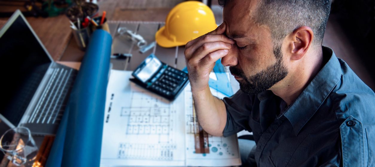 Avoid these KPI pitfalls when you use Construction software for tracking KPIs | B3 Software Overworked stressed construction worker frustrated as he looks at blueprints