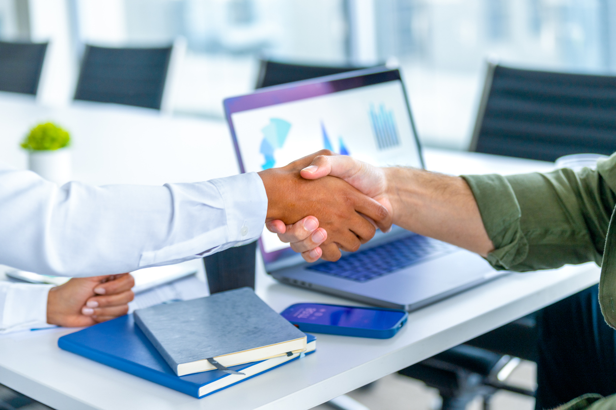 two hands shaking over a laptop screen that shows custom software
