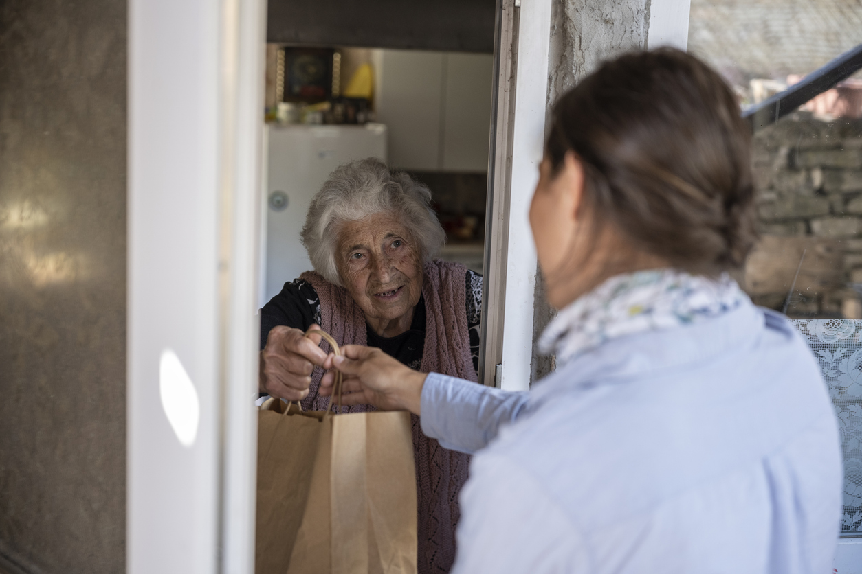 Image of meals on wheels interaction where an employee is handing off food to an elderly woman.